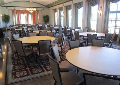 An empty Rackham Building banquet hall with round tables and chairs neatly arranged on a patterned carpet.