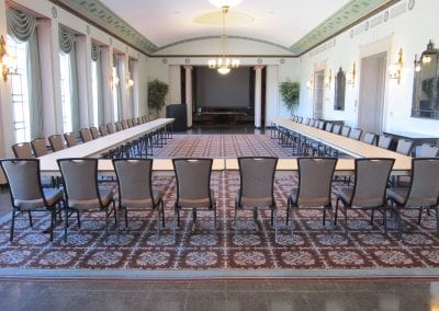 A spacious conference room with a long rectangular table surrounded by chairs, adorned with elegant carpeting and classical decor.