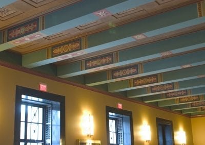 Ornately decorated ceiling with patterned designs, wall sconces, and windows in a stately lobby of the Rackham Building.