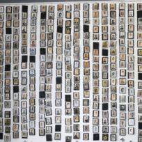 A wall covered with numerous small, black-and-white and colored portrait photographs of various individuals arranged in a grid-like pattern.