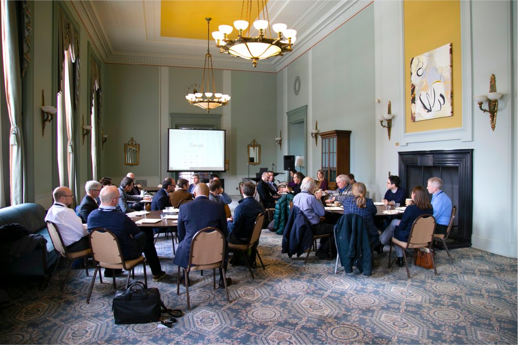 People discuss at tables in the West Study Lounge of the Rackham Building