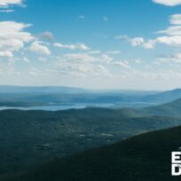 Aerial view of a vast landscape with green hills, a large lake, and a sky filled with scattered clouds. The text "Earth Day at 50" is in the bottom right corner.