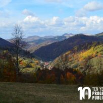A scenic view of a valley with autumn foliage, distant hills, and a village. "Ten Years Program in Public Scholarship" is displayed in the image corner.