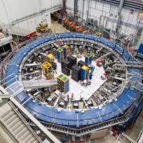 A large, circular particle accelerator with electronic equipment in the center, surrounded by metal walkways and cables inside a laboratory facility.