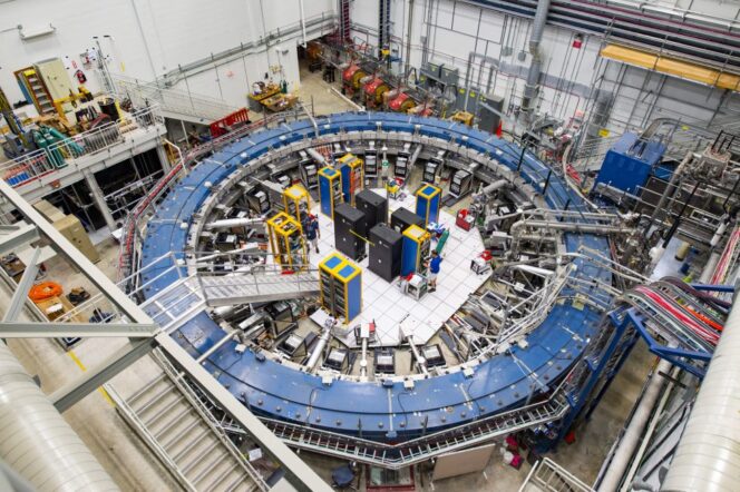 A large, circular particle accelerator with electronic equipment in the center, surrounded by metal walkways and cables inside a laboratory facility.