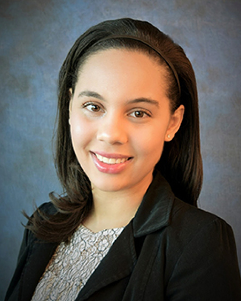 Patrice Hicks smiles in front of a photo studio backdrop.