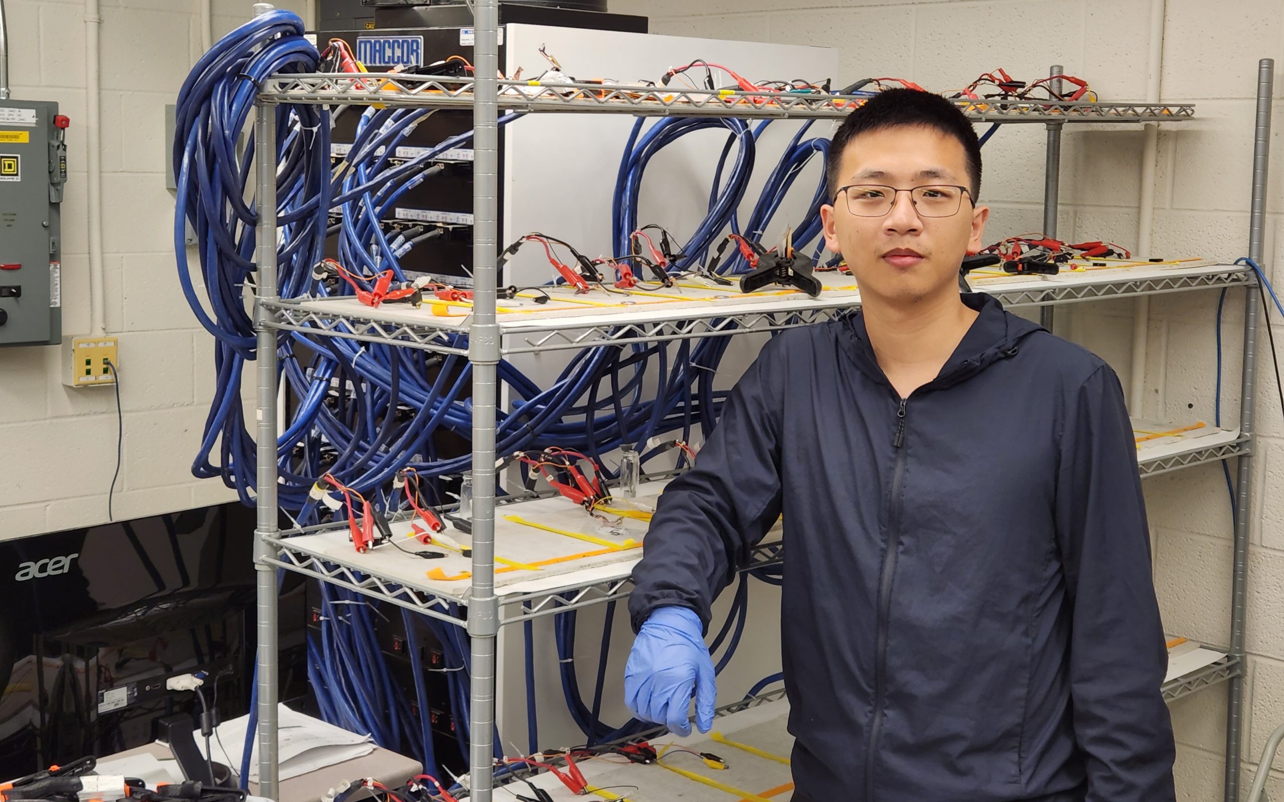 Changyu Deng stands beside batteries being tested in the lab.