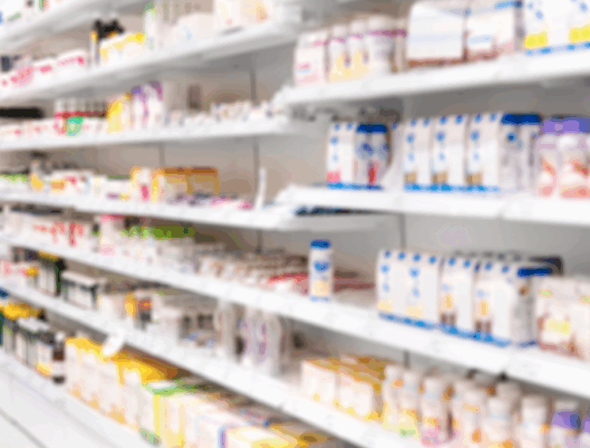 Blurred image of pharmacy shelves stocked with various bottles and boxes of health products and medications.