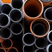 A top-down view of stacked plastic pipes in various sizes, with gray and orange exteriors, arranged closely together.