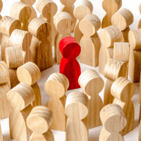 A group of wooden human-shaped figures surrounds a single red figure, highlighting contrast and individuality.