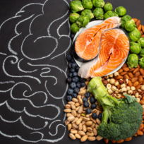 Salmon, nuts, berries, broccoli, and Brussels sprouts arranged to resemble a brain on a blackboard, with a chalk outline on the left side.