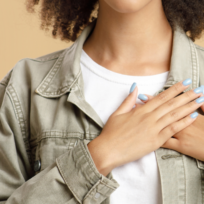 Person with curly hair, wearing a denim jacket and white shirt, places hands on chest.