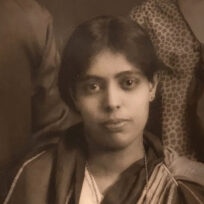 A sepia-toned portrait of a young woman with short hair, wearing a traditional outfit. She is gazing directly at the camera with a neutral expression.