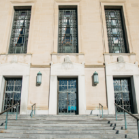 The image shows the front facade of a historic building with tall windows, three entrance doors, and a series of steps leading up to it.