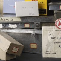 A collection of labeled boxes and metal cases with various labels, including an envelope addressed to the University of Michigan Library from the British Museum, London.