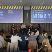 A panel discussion on careers in media and film with four speakers seated on stage, facing an audience in a lecture hall. Presentation screens display names and roles of the participants.