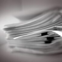 A blurred stack of papers or documents, arranged in a slightly fanned out manner, resting on a flat surface.