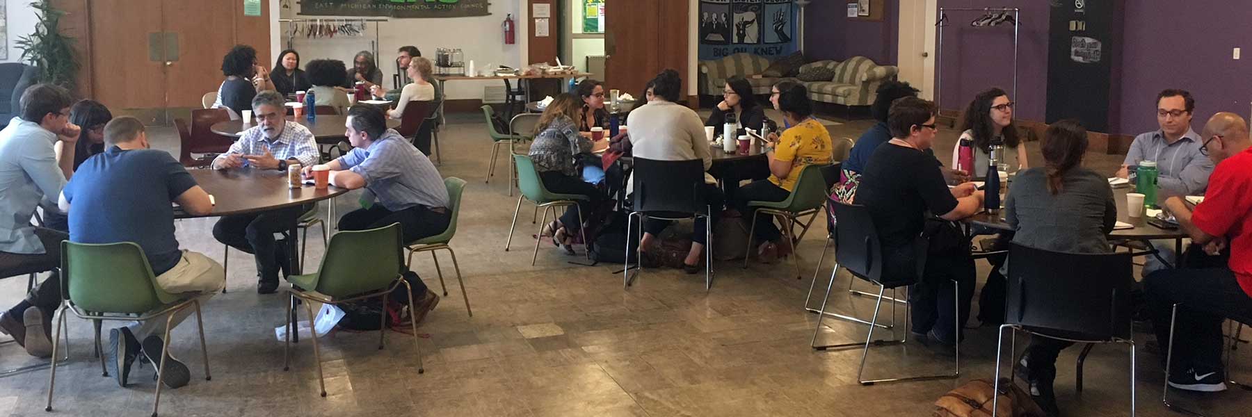 People sitting at tables in a communal area, engaged in conversation, with food and drinks on the tables.