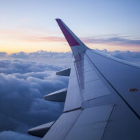 Airplane wing against a backdrop of clouds at sunset, showing a gradient of colors from orange to blue across the sky.