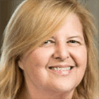 A middle-aged woman with blonde hair smiles at the camera against a neutral background.