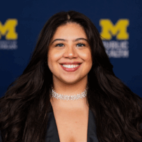 A headshot of Andrea Valenzuela, dressed in a navy blue blazer with a sparkly necklace.