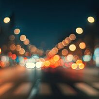 Blurred city street at night with out-of-focus car headlights, streetlights, and traffic signals creating colorful bokeh effects.