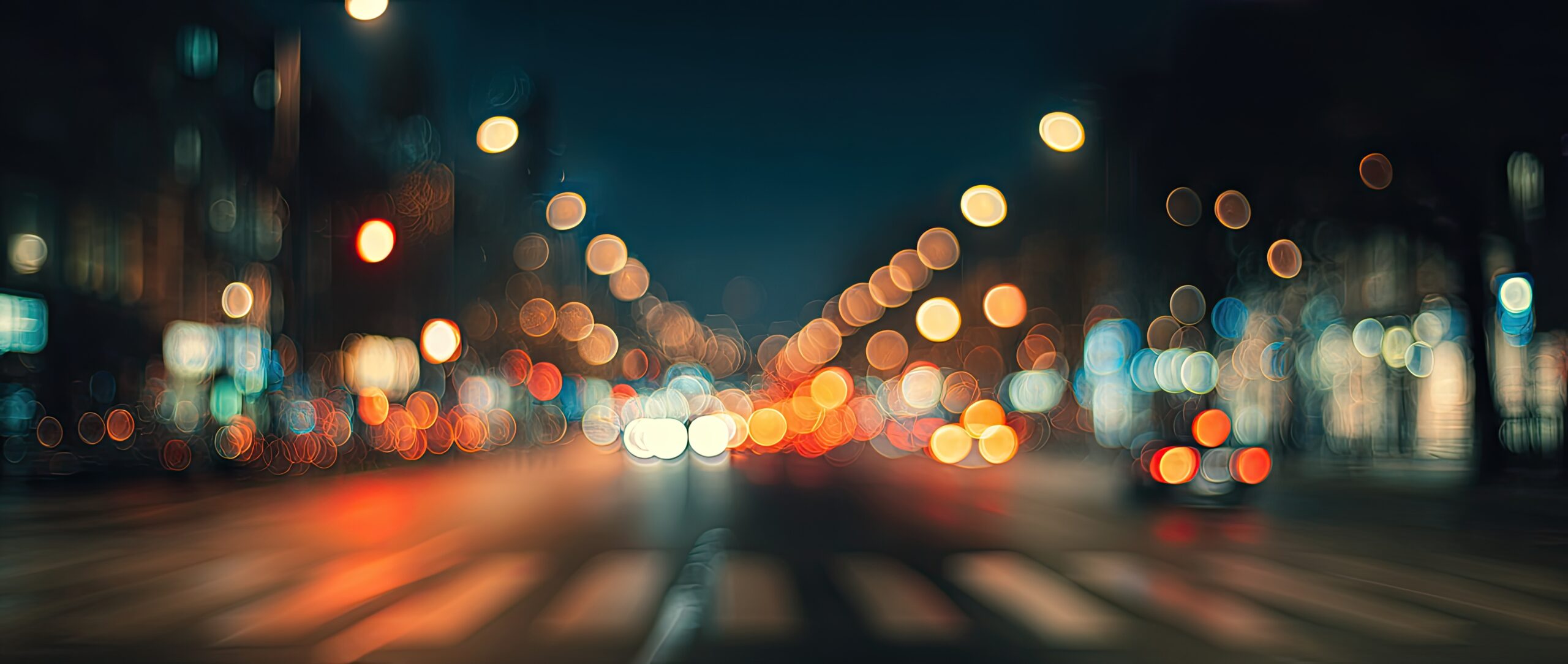 Blurred city street at night with out-of-focus car headlights, streetlights, and traffic signals creating colorful bokeh effects.