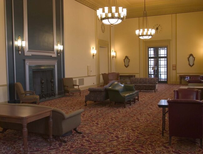 A spacious, traditional lounge with upholstered chairs, sofas, chandeliers, a fireplace, and patterned carpeting.