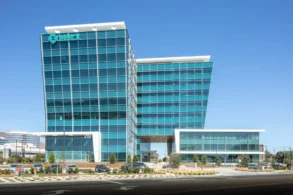 A modern glass office building with the Merck logo displayed at the top, set against a clear blue sky with parked cars in front.