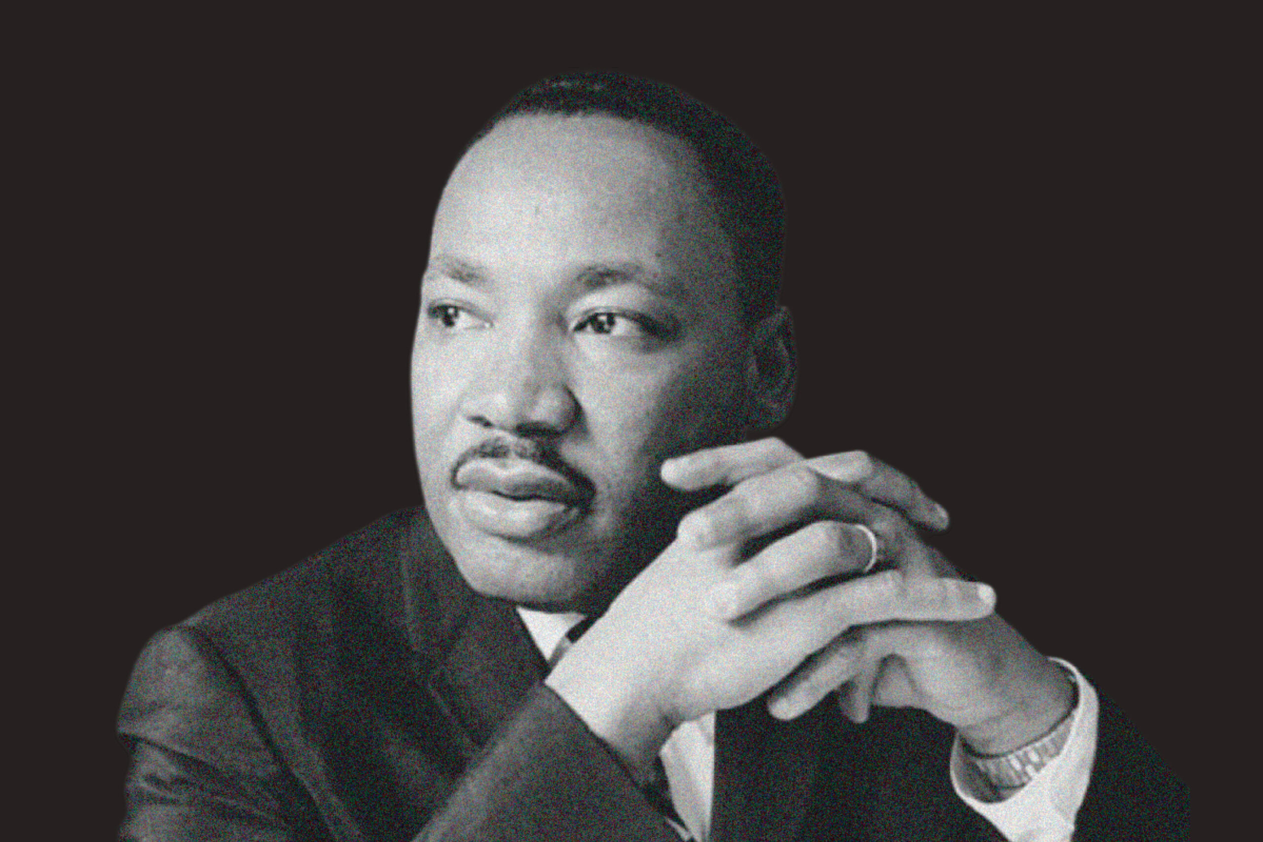 A man in a suit sits with his hands clasped, gazing to the side against a dark background.