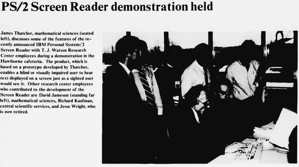 A group of people observe a man seated at a table demonstrating an IBM PS/2 screen reader in a cafeteria setting, as part of a research presentation.