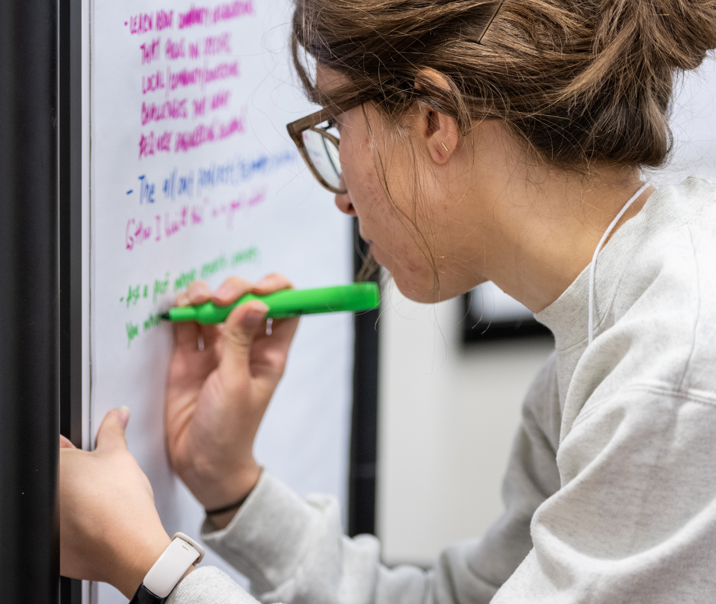 A person wearing glasses writes on a large sheet of paper with a green marker. The paper contains notes written in multiple colors.