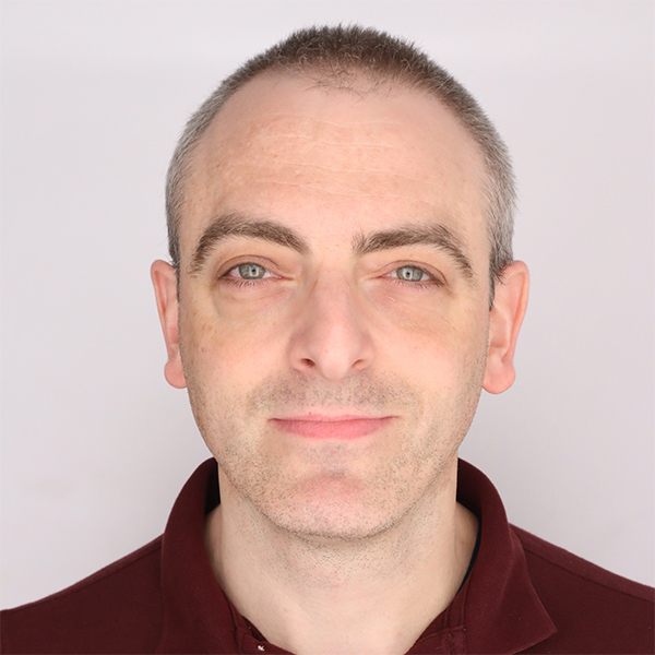 A man with short brown hair and blue eyes, wearing a maroon collared shirt, faces the camera against a plain light background.