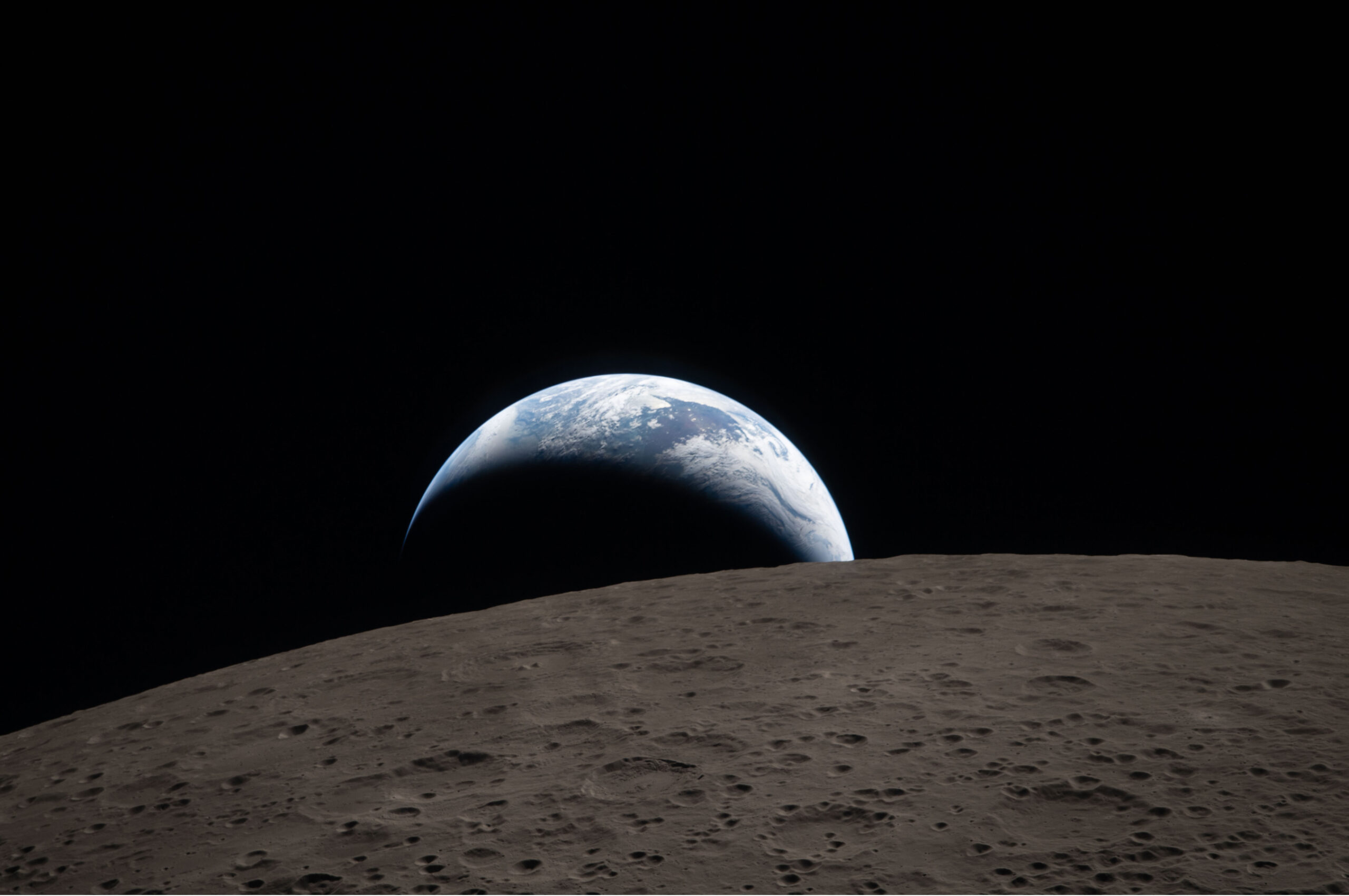 A view of Earth rising over the horizon of the Moon, with the lunar surface in the foreground and the dark space in the background.