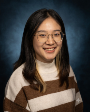 A woman with shoulder-length dark hair, wearing glasses and a brown and white striped sweater, smiles at the camera against a dark blue background.