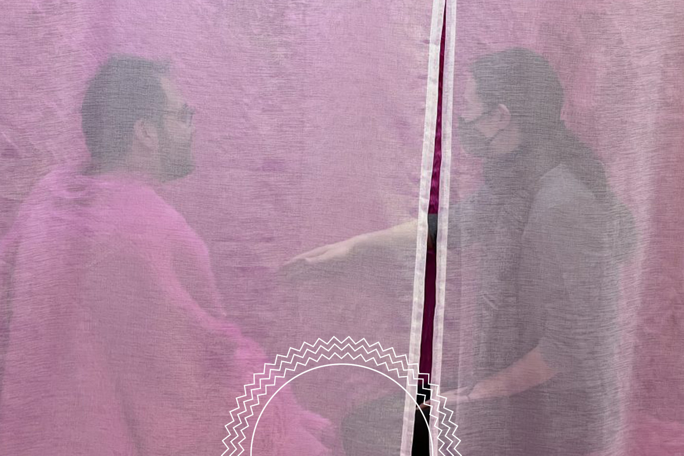 Two people wearing face masks and glasses sit facing each other, separated by a pink translucent curtain, with one person reaching out a hand.