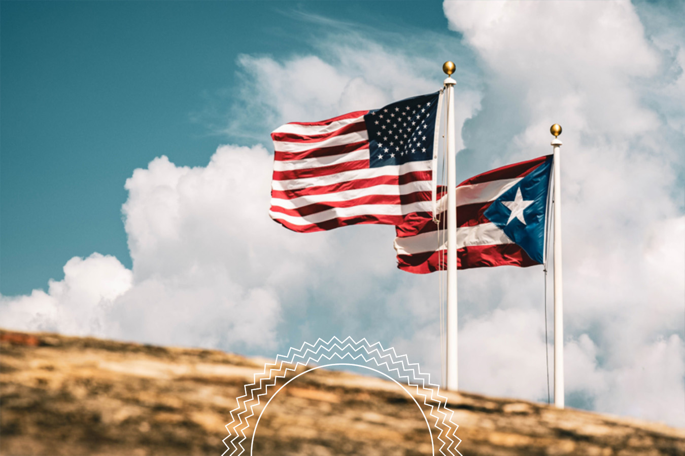 The United States flag and the Puerto Rico flag fly on flagpoles against a partly cloudy sky, with a rock formation in the foreground.