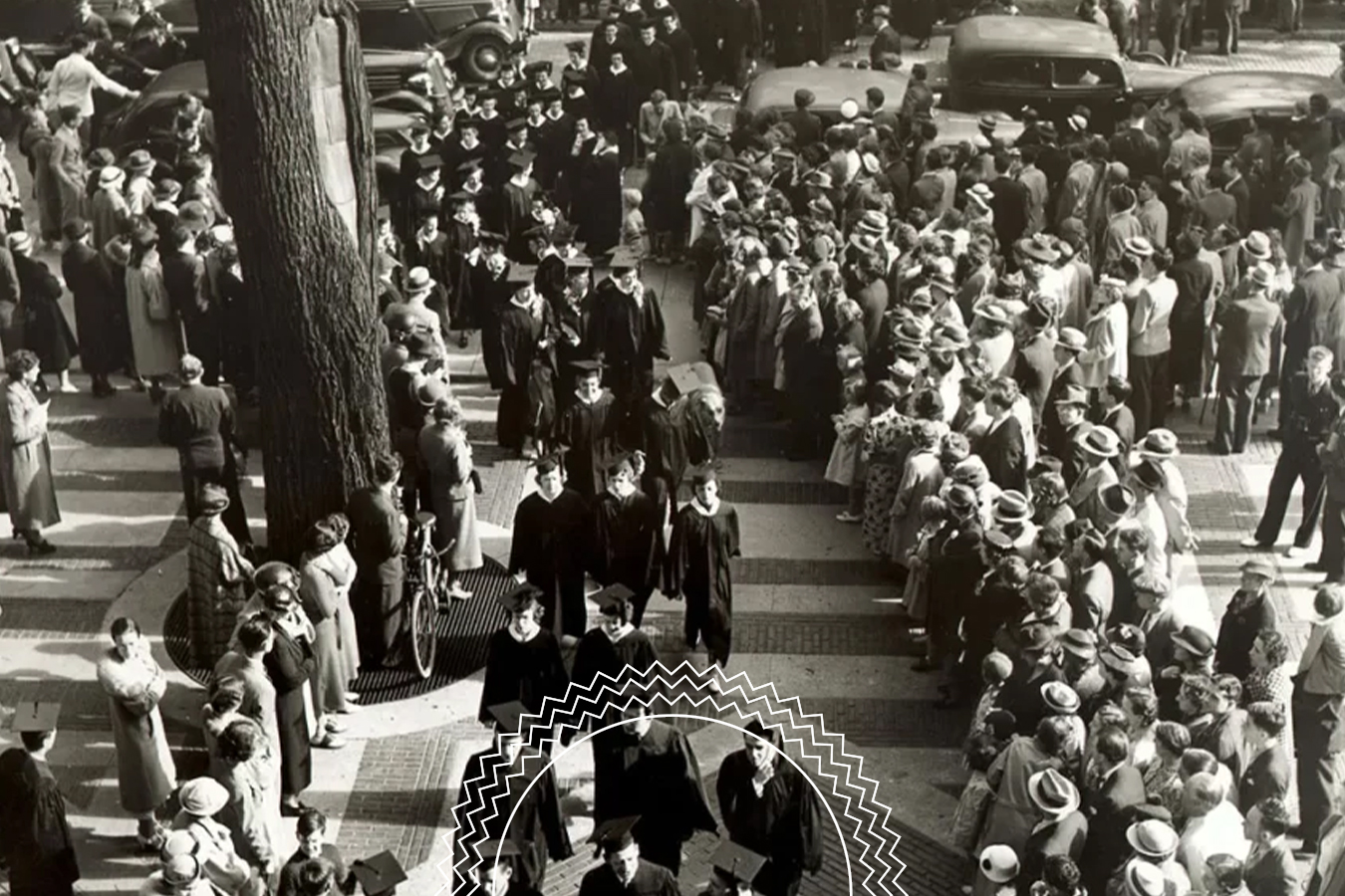 A black-and-white photo shows people in formal attire walking in a procession as crowds line the street, watching from the sidewalk; vintage cars are visible in the background.