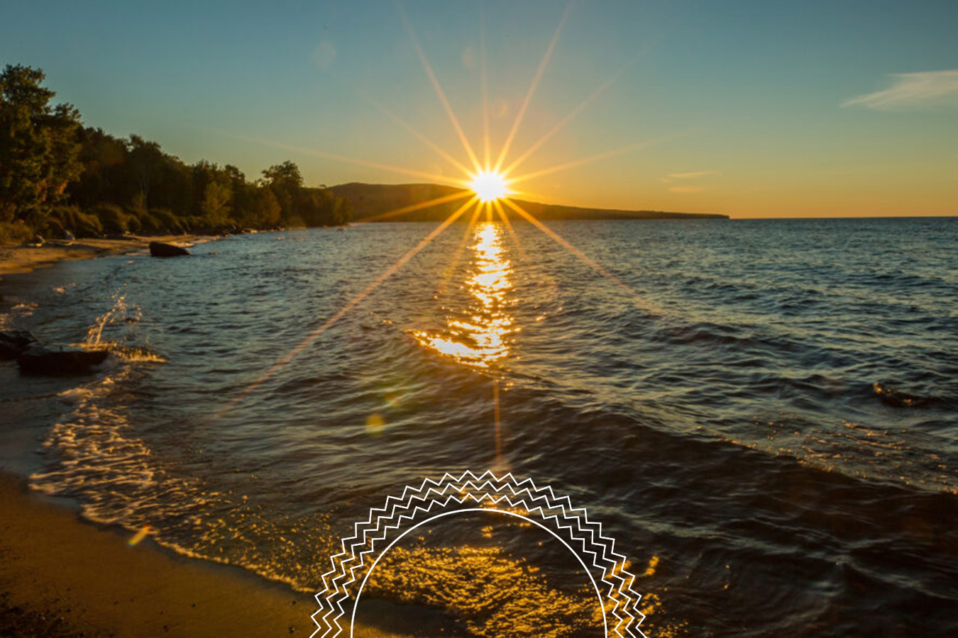 The sun sets over a calm lake, casting reflections on the water near a shoreline lined with trees under a clear sky.
