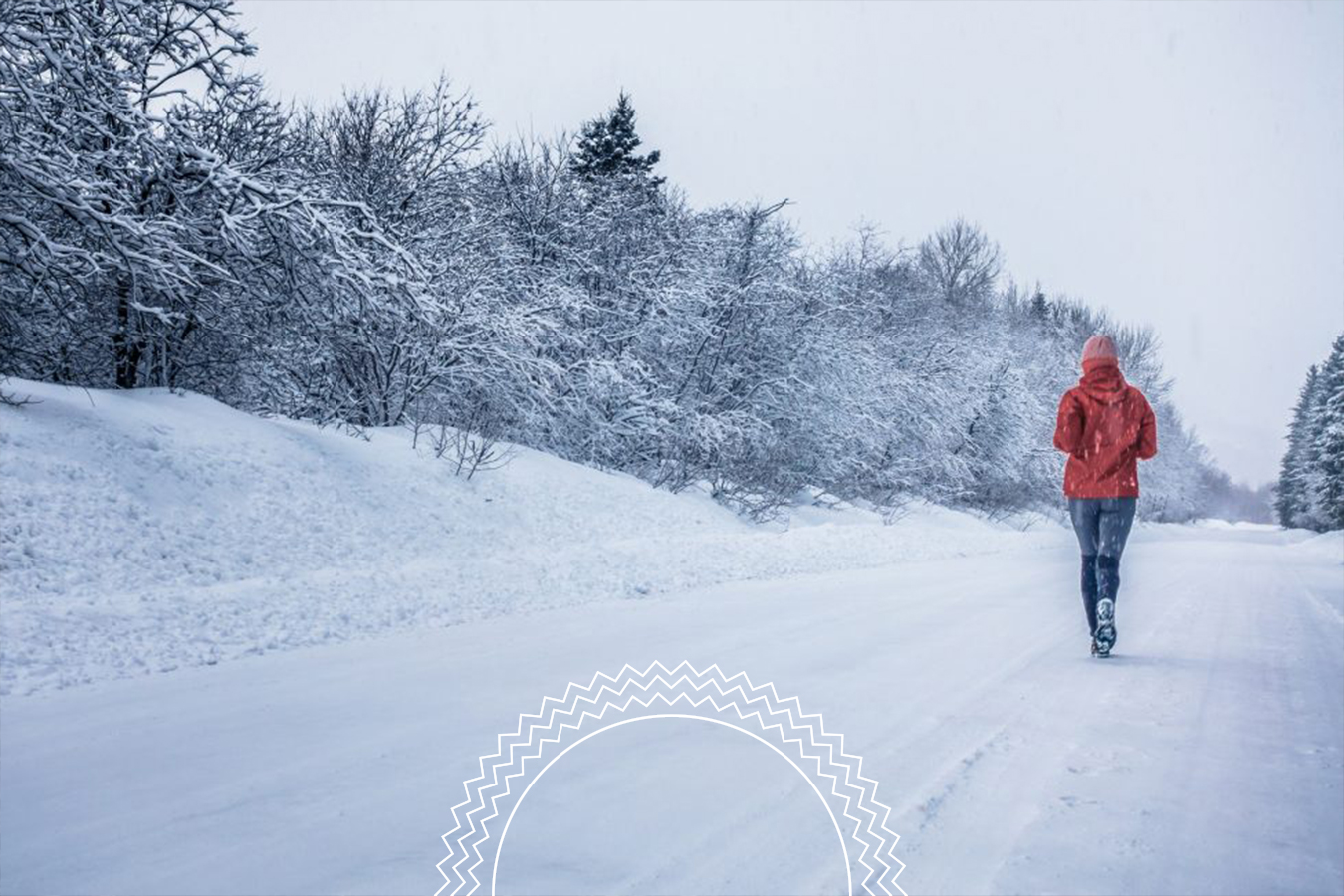 A person wearing a red jacket jogs on a snow-covered road lined with trees during winter.