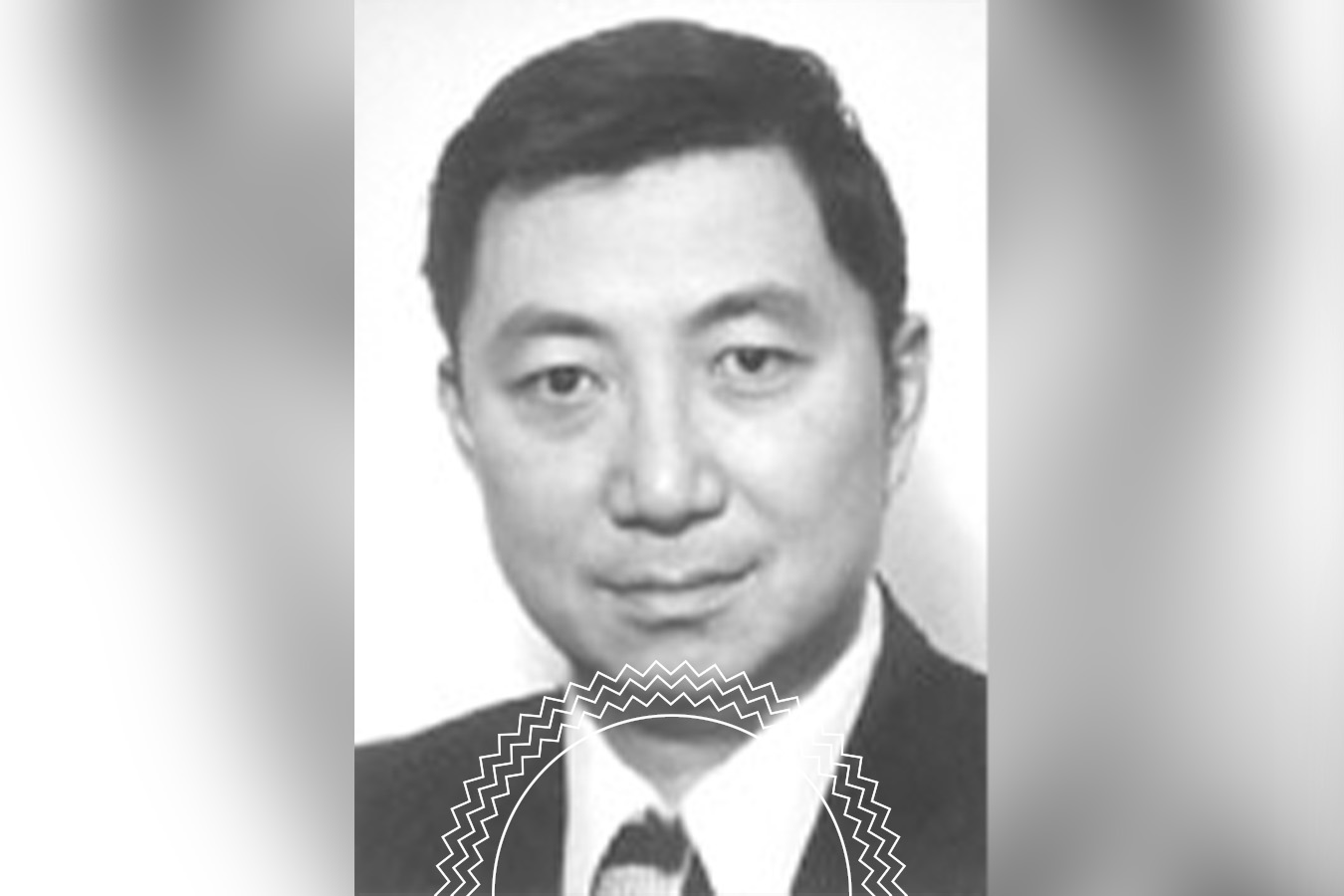 Black and white portrait of a man in a suit and tie, facing the camera with a neutral expression; background is plain and blurred at the edges.