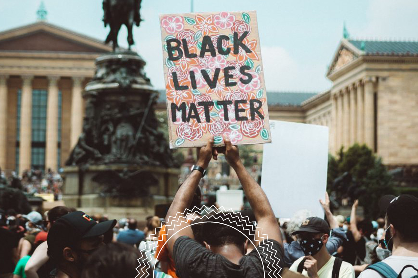 A person holds a colorful “Black Lives Matter” sign above their head in a crowd of protesters outside a large historic building.