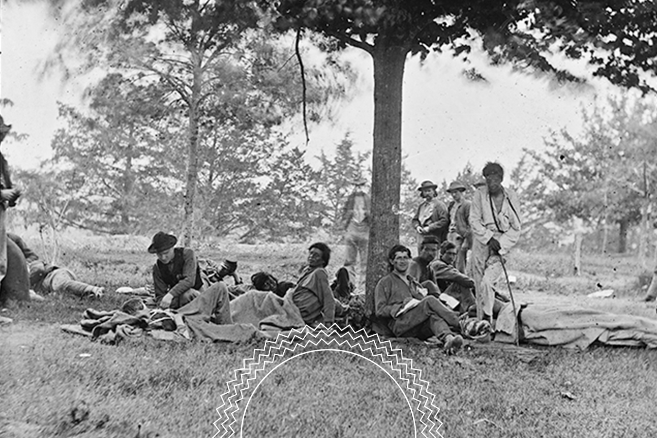 A group of men in 19th-century clothing sit and stand under a tree on a grassy area, with blankets and belongings on the ground.