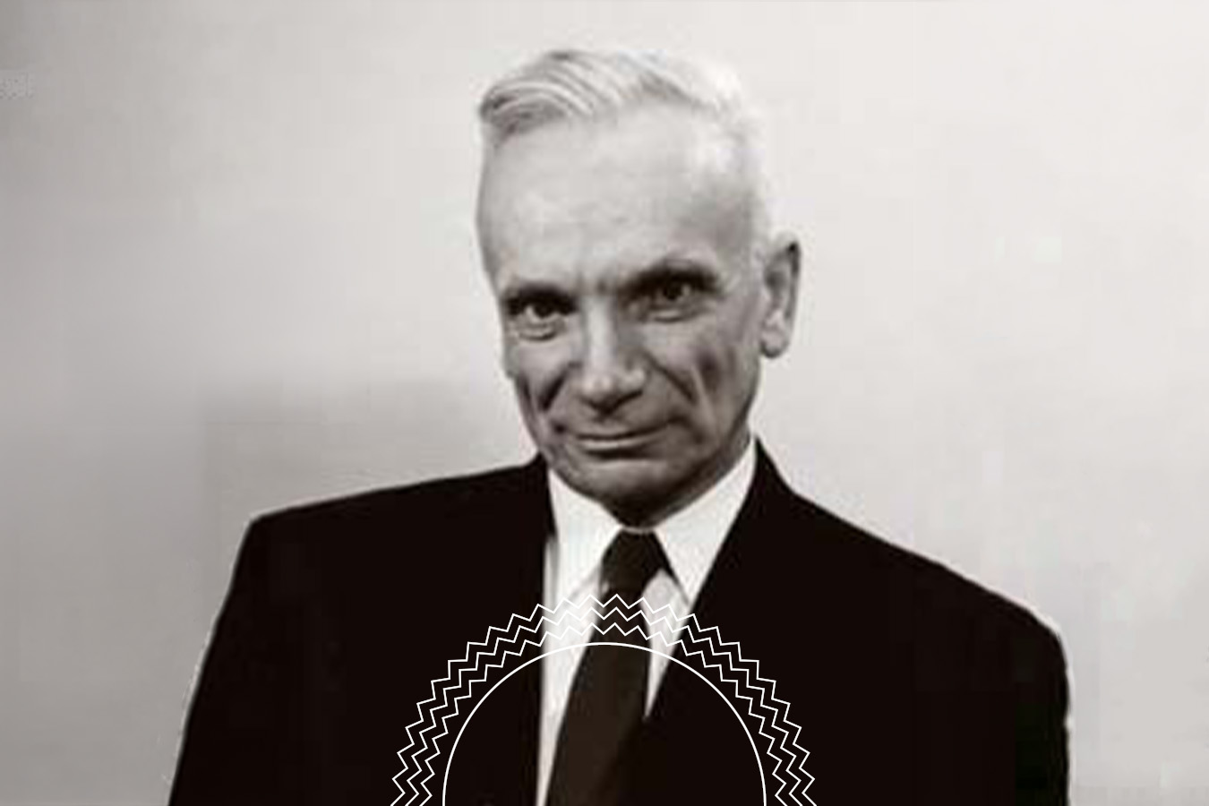 Black and white portrait of an older man in a suit and tie, with short, neatly combed hair, standing against a plain background.