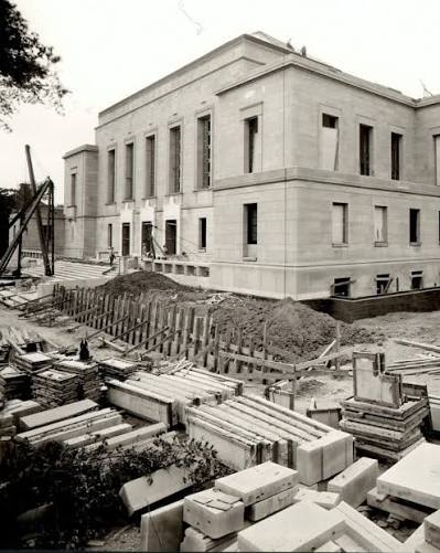 A large stone building under construction, with scaffolding, construction materials, and workers visible around the site.