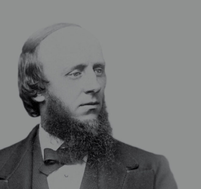 Black-and-white portrait of a man with a receding hairline, sideburns, and a full beard, wearing a suit and bow tie, looking slightly to his left.