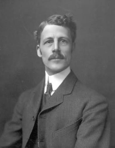 Black and white portrait of a man with a mustache, wearing a suit and tie, looking slightly to the side against a plain background.