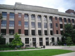 A four-story brick and stone university building with a central portico supported by tall columns.